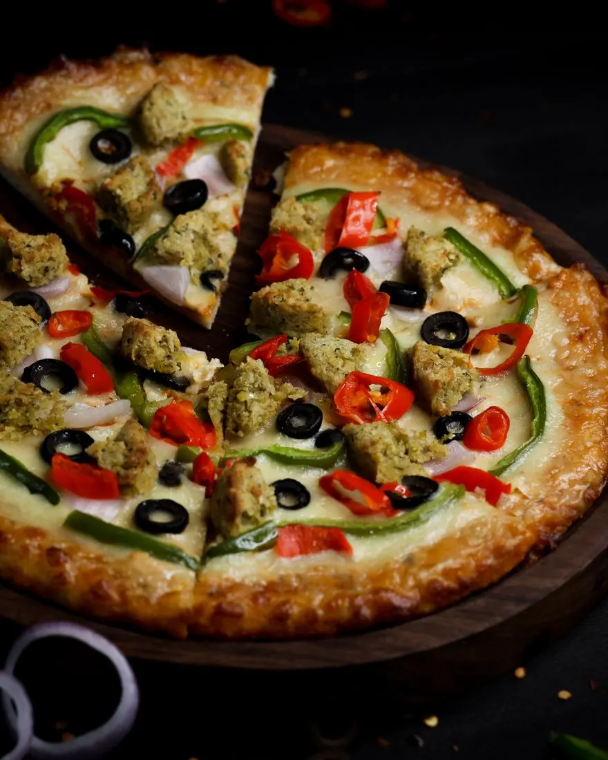 Whole pizza with vegetables and olives on a dark surface